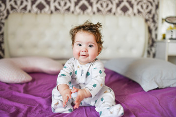 the baby is sitting on the bed. Cute girl on the bed in the bedroom