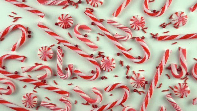 Close up of Christmas Eve season red color mood table with candy canes and peppermint spinning over white background. Holiday scene with pearls sprinkles.
