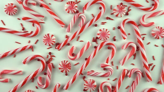Close up of Christmas Eve season red color mood table with candy canes and peppermint spinning over white background. Holiday scene with pearls sprinkles.