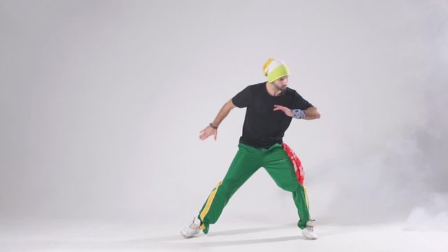 Handsome young professional hip hop dancer performing on stage of dance school, preparing for concert, training hard in smoky dark studio