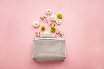 white and green little flowers in a gray cosmetic bag on a pink background. cute feminine postcard