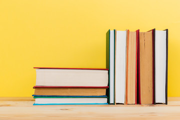 Simple composition of many hardback books, raw of books on wooden table and pastel yellow background