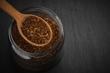 Obraz na płótnie Canvas Open jar with instant coffee and spoon with coffee closeup on black stone background