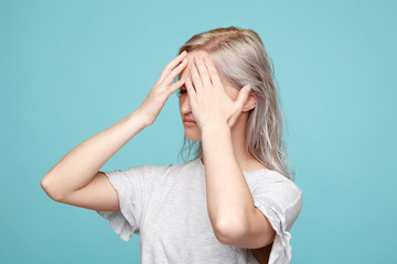 Unhappy young lady in stress with headache holding her head by hand isolated in the blue studio