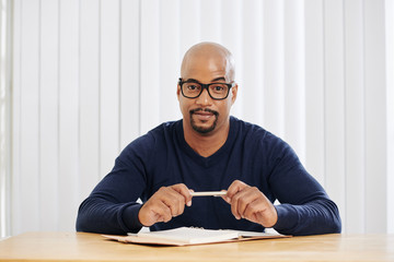 Positive bald man with circle beard sitting at desk and taking notes in planner