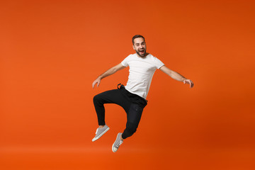 Fototapeta na wymiar Cheerful excited young man in casual white t-shirt posing isolated on bright orange wall background studio portrait. People lifestyle concept. Mock up copy space. Having fun, fooling around, jumping.
