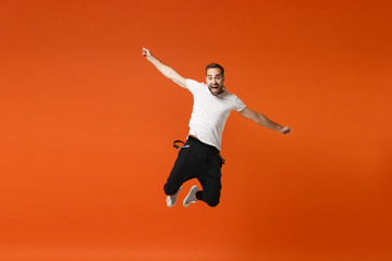 Joyful young man in casual white t-shirt posing isolated on orange wall background studio portrait. People sincere emotions lifestyle concept. Mock up copy space. Having fun jumping, spreading hands.