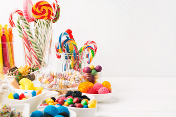 Different colorful candy sweets. Mix candy confectionery in jars on white wooden background with...