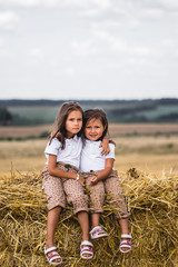 Naklejka na ściany i meble Two girls sitting on a bale of hay