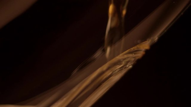 Beer poured against inside of glass in dark room, extreme close-up