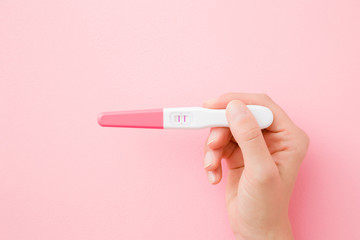 Fototapeta Young woman hand holding pregnancy test with two stripes on pastel pink background. Positive result. Closeup. Point of view shot. Top down view. obraz