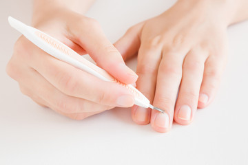 Woman hand removing nail cuticle with pusher stick on light gray table. Care about dry, overgrown cuticle. Front view. Close up.