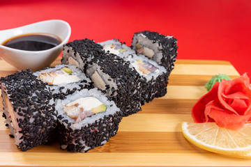 Sushi, rolls in black sesame, with cheese, shrimp, and crab. On the plank. On a red background.