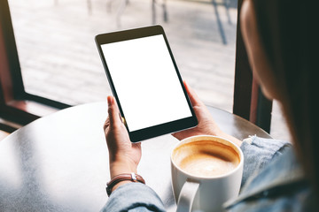 Mockup image of a woman holding black tablet with white blank screen and coffee cup on the table