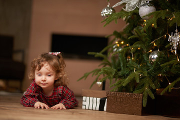 Merry girl near the festive Christmas tree celebrates Christmas, gifts, holiday, warm
