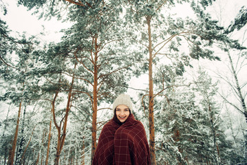 Young pretty girl under a brown plaid in a snowy pine forest. Winter mood.