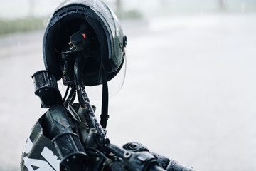 Fototapeta na wymiar Wet black helmet hanging on handlebar of motorcycle on rainy day
