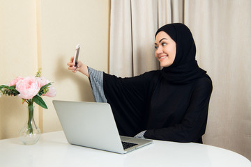 Portrait of a young attractive woman in hijab making selfie photo on smartphone.