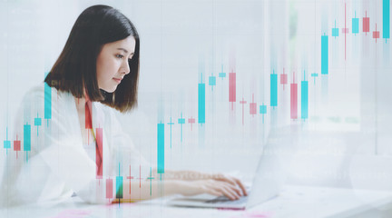 Double exposure young asian business woman working on computer laptop in office room with paperwork document on desk. Technical price candlestick chart graph and indicator stock trading
