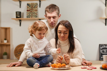 Cheerful loving family with a child in the kitchen, celebrate Christmas, New Year. Eat tangerines