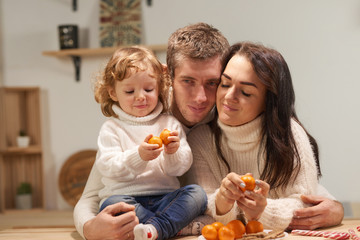 Cheerful loving family with a child in the kitchen, celebrate Christmas, New Year. Eat tangerines