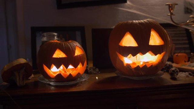 Jack-o'-lanterns on a wooden furniture. Beautiful fresh carved pumpkins close up lit with candles. Typical scary halloween decoration, October 31. 4K professional night handheld footage.