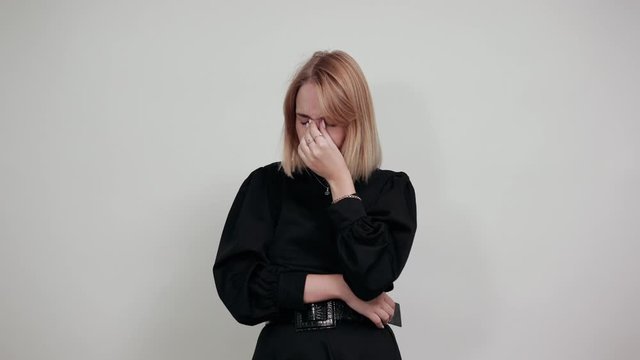 Portrait of tired young lady in black casual shirt keeping eyes closed and putting hand on nose isolated on brignt white background in studio. People lifestyle concept.