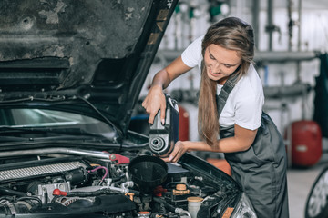 Beautiful Mechanic  girl in a black jumpsuit and a white T-shirt changes the oil in a black car