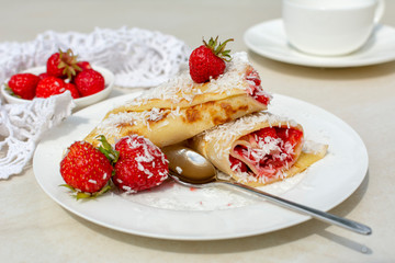 Rolled crepes or balkan pancakes stuffed fresh chopped strawberries, decorated powdered sugar and coconut flakes . Gourmet sweet dish