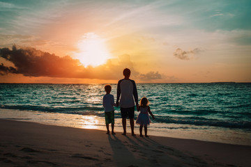 father and kids walking on beach at sunset