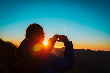 tourist enjoy sunset in mountains, making heart with hands
