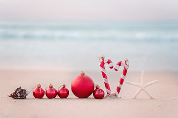 Fototapeta na wymiar Christmas ball and starfish on yellow sand and sea background. New Yeaar or Xmas holiday vacation in exotic countries or tropics concept: christmas decorations on the beach. Copy space for text