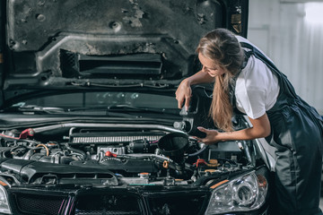 Fototapeta na wymiar Beautiful Mechanic girl in a black jumpsuit and a white T-shirt changes the oil in a black car. car repair concept