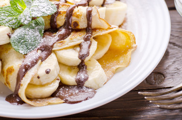 French crepes with chocolate sauce and banana in ceramic dish on wooden kitchen table