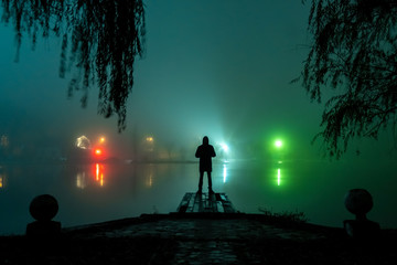 silhouette of a man and a lake in the fog at night
