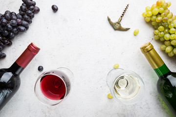 Glasses of white and red wine with ripe grapes on stone background, top view