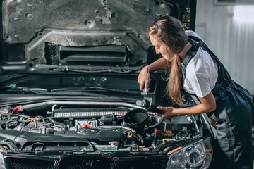 Beautiful Mechanic  girl in a black jumpsuit and a white T-shirt changes the oil in a black car. car repair concept