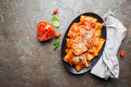 Pasta paccheri with tomato sauce and basil in a plate, top view