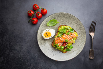 Toast with avocado cream and smoked salmon over black background, top view