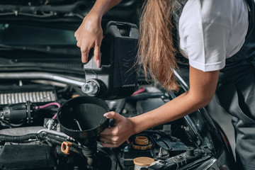Plakat Beautiful Mechanic girl in a black jumpsuit and a white T-shirt changes the oil in a black car.close up photo. car repair concept