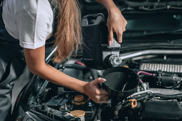 Beautiful Mechanic  girl in a black jumpsuit and a white T-shirt changes the oil in a black car.close up photo. car repair concept