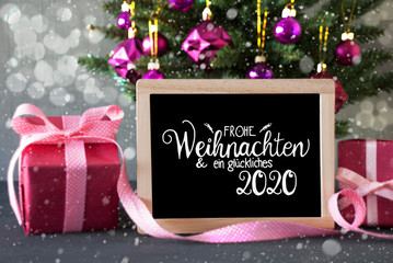 Blackboard With German Calligraphy Frohe Weihnachten Und Ein Glueckliches 2020 Means Merry Christmas And Happy 2020. Christmas Tree With Purple Ball Ornament, Pink Gift And Bokeh Effect And Snowflakes