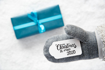 Label With English Calligraphy Merry Christmas And A Happy 2020. Gray Glove With Turquoise Gift And Snow Background