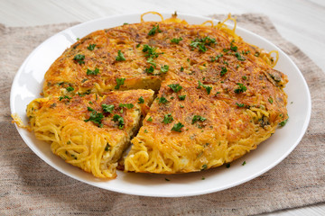 Homemade spaghetti omelette on a white plate, side view. Close-up.