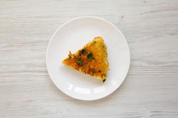 A piece of spaghetti omelette on a white plate on a white wooden background, overhead view. Flat lay, top view, from above.