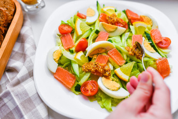 add mustard to vegetable salad. vegetable salad with human hands. on a white plate. add spices.