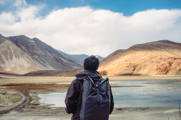 Young wanderlust traveler with backpack against Pangong Lake in Leh, Ladakh, India. Travel trip and Tourism concept background.
