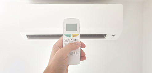 Fototapeta premium Modern airconditioner unit with a hand holding a remote.