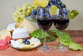 Glasses of red wine against blue grapes and various cheese