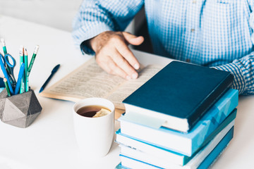man reading book on modern stylish work place with office supplies, glasses, notebooks and books, desk work concept in white and blue colors.
